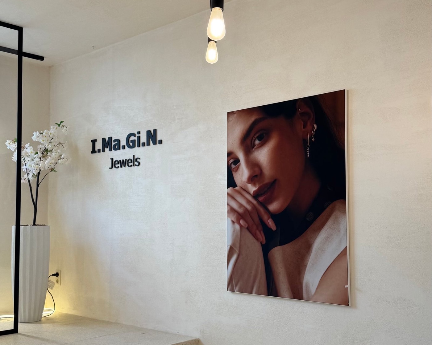 An I.Ma.Gi.N. Jewels store interior, with the brand name on the wall beside a portrait of a curated ear